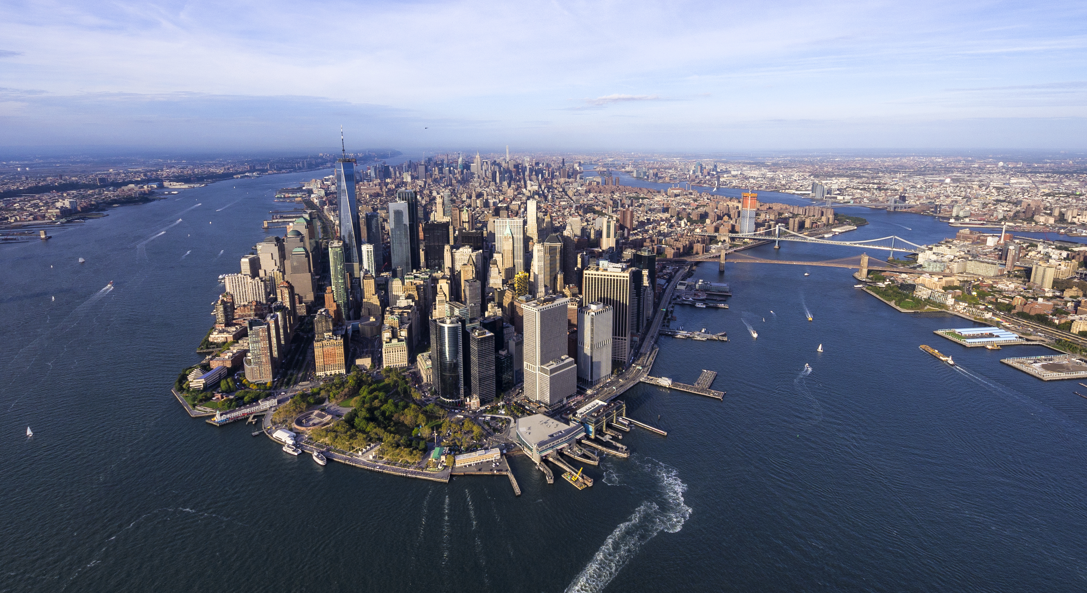 Aerial view of Lower Manhattan, New York City, showing skyscrapers, waterfront parks, and surrounding rivers with boats. The Brooklyn and Manhattan bridges are visible in the background. Photo by Eloi Omella/Getty Images.