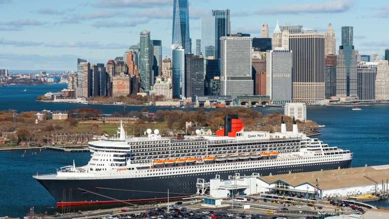 Aerial view of a large cruise ship docked at the Brooklyn Cruise Terminal with the New York City skyline, including One World Trade Center, visible across the river on a clear day. Photo by C. Taylor Crothers/NYCEDC.