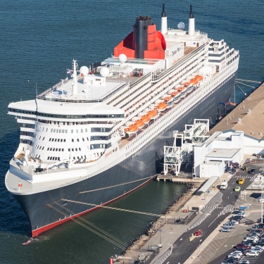A large cruise ship is docked at Brooklyn Cruise Terminal, with parked cars nearby, and calm blue water surrounding the ship. Photo by C. Taylor Crothers.